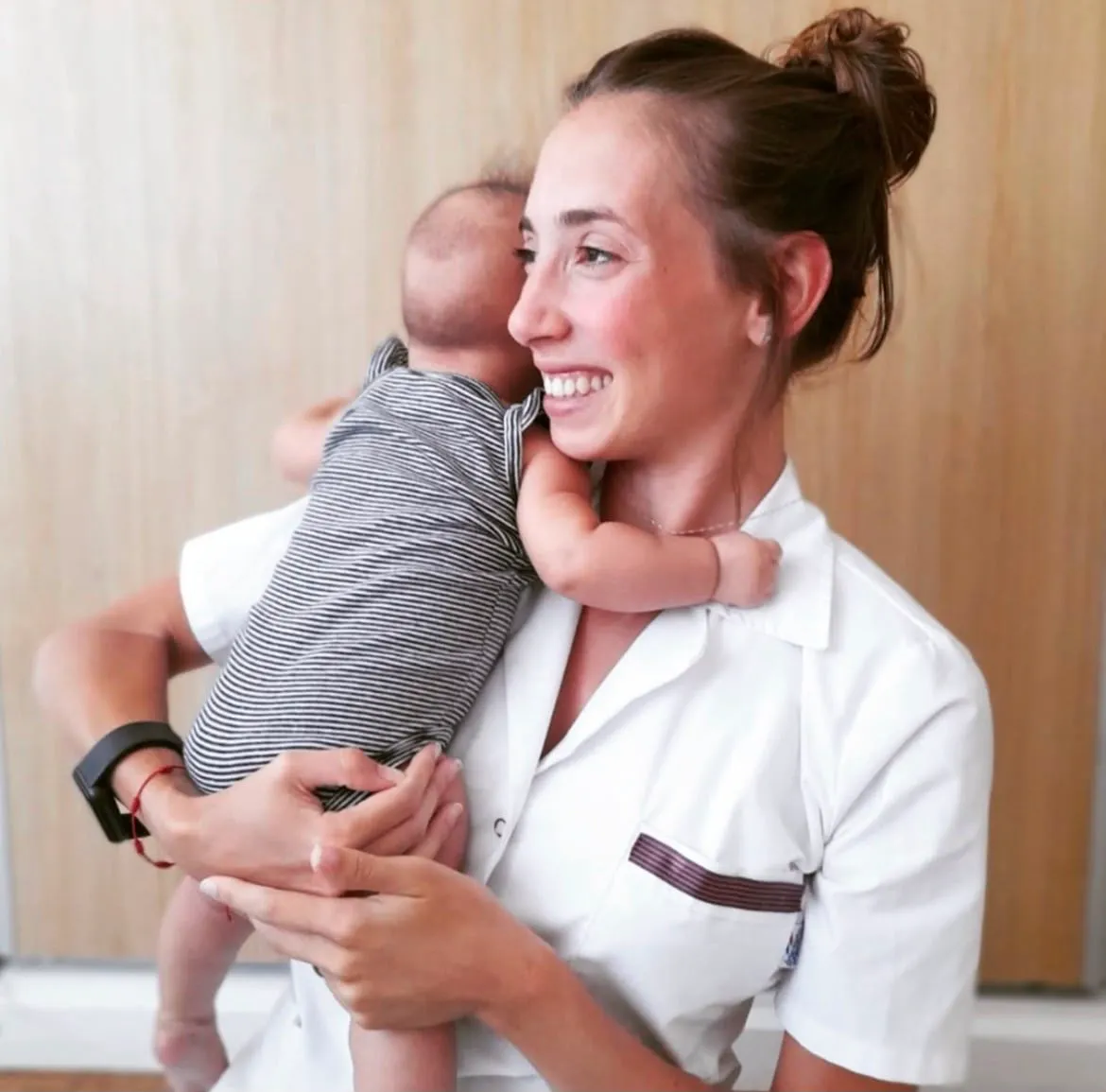 Mica Di Pierro, nutricionista, en guardapolvo sonriendo mientras sostiene a un bebé en brazos